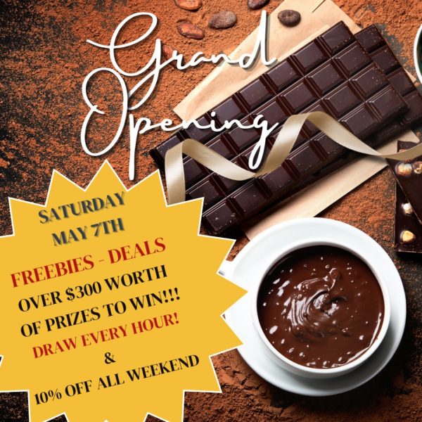 A wooden table holds a chocolate bar, a chocolate drink and the words grand opening with details about the Petite Patrie grand opening