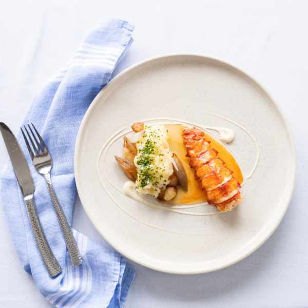 lobster with shallot butter on white plate with fork and light blue napkin