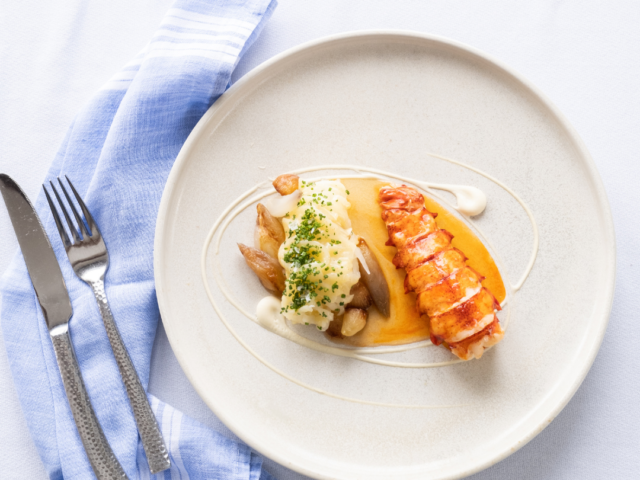 lobster with shallot butter on white plate with fork and light blue napkin