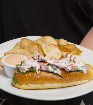 hands hold a lobster roll on a plate