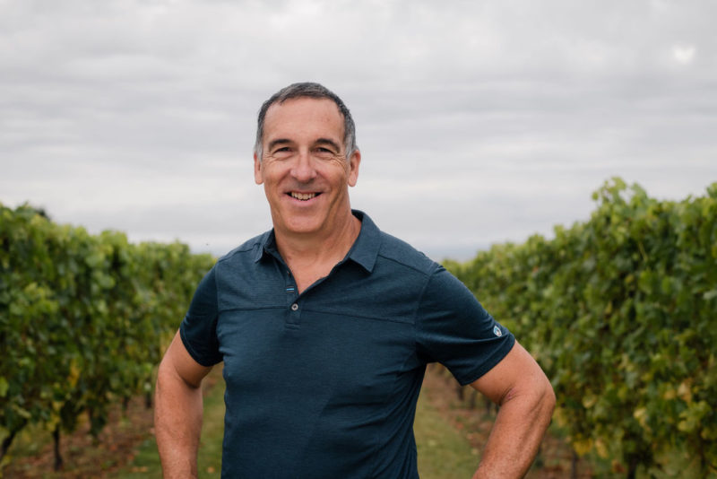 A photo of Hans Christian Jost. He is standing outside in a vineyard with a gray sky behind him.