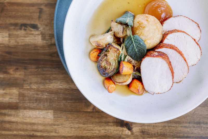 A photo of a plate on a wooden surface. The plate is aligned to the upper right hand corner of the photo and has carrots, brussels sprouts and a protein on the plate.