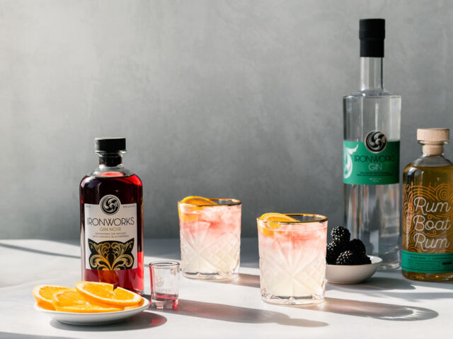 A photo of the Harbour Sunset cocktail. There are three bottles of Ironworks products and two glasses of the cocktail.