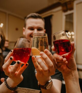 A photo of three people clinking their glasses together in cheers at the 2022 Ciders and Sliders event.
