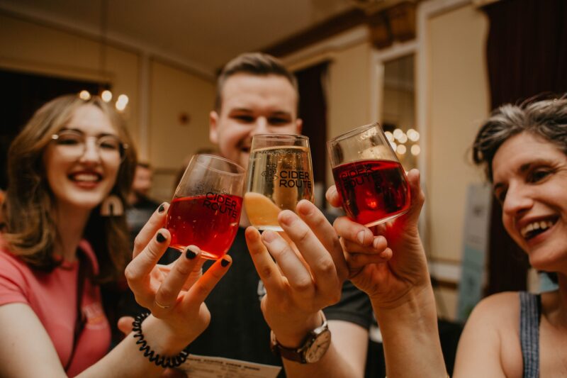 A photo of three people clinking their glasses together in cheers at the 2022 Ciders and Sliders event.