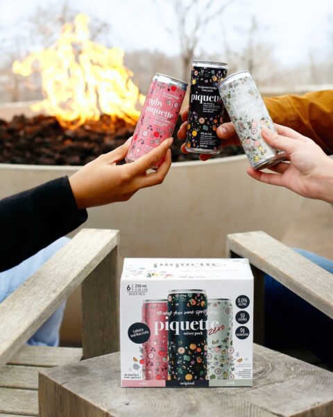 A photo of a trio of Benjamin Bridge's Piquette Zero products. There are three hands showing, each holding a different can.