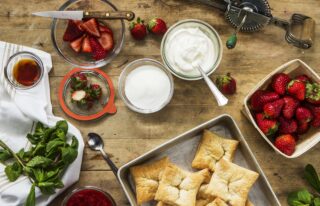 Photo of square puff pastries on a metal sheet beside mowls of sugar, yogurt, and strawberries